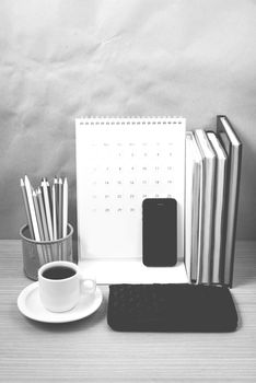 office desk : coffee with phone,wallet,calendar,color pencil box,stack of book on wood background black and white color