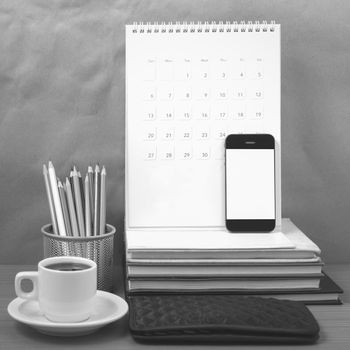 office desk : coffee with phone,wallet,calendar,color pencil box,stack of book on wood background black and white color