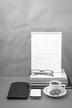 office desk : coffee with phone,wallet,calendar,heart,stack of book,eyeglasses on wood background black and white color