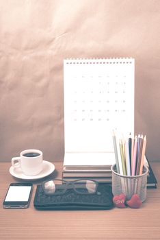 office desk : coffee with phone,wallet,calendar,color pencil box,stack of book,heart,eyeglasses on wood background vintage style