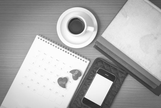 office desk : coffee with phone,wallet,calendar,heart,stack of book on wood background black and white color