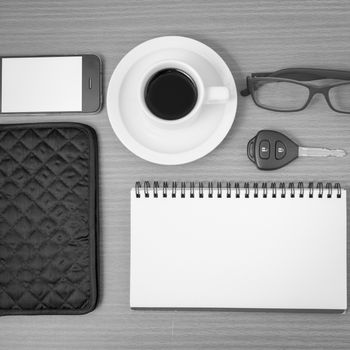 coffee and phone with notepad,car key,eyeglasses and wallet on wood table background black and white color