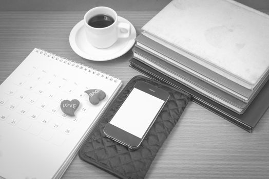 office desk : coffee with phone,wallet,calendar,heart,stack of book on wood background black and white color