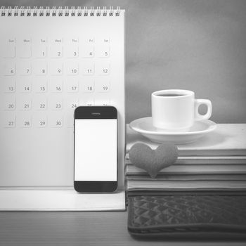 office desk : coffee with phone,wallet,calendar,heart,stack of book on wood background black and white color