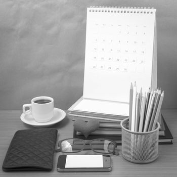 office desk : coffee with phone,wallet,calendar,color pencil box,stack of book,heart,eyeglasses on wood background black and white color