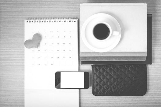 office desk : coffee with phone,wallet,calendar,heart,stack of book on wood background black and white color