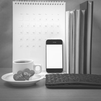 office desk : coffee with phone,wallet,calendar,heart,stack of book on wood background black and white color