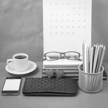 office desk : coffee with phone,wallet,calendar,color pencil box,stack of book,heart,eyeglasses on wood background black and white color