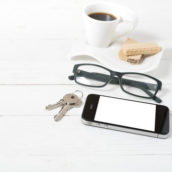 coffee cup with wafer,phone,key,eyeglasses on white wood background