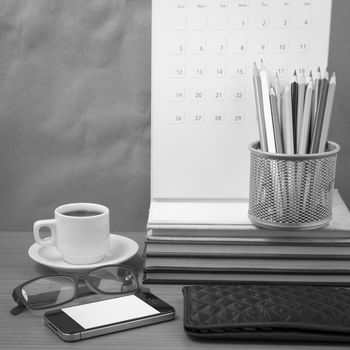 office desk : coffee with phone,wallet,calendar,color pencil box,stack of book,eyeglasses on wood background black and white color