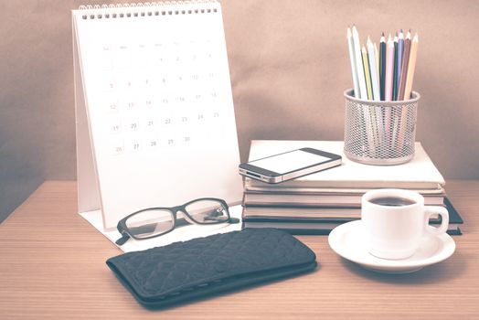 office desk : coffee with phone,wallet,calendar,color pencil box,stack of book,eyeglasses on wood background vintage style