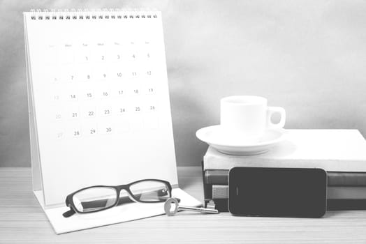 coffee and phone with key,eyeglasses,stack of book,calendar on wood background black and white color