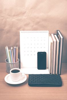 office desk : coffee with phone,wallet,calendar,color pencil box,stack of book on wood background vintage style