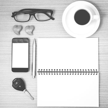 office desk : coffee and phone with car key,eyeglasses,notepad,heart on wood background black and white color