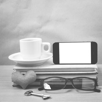 office desk : coffee and phone with key,eyeglasses,stack of book,heart on wood background black and white color