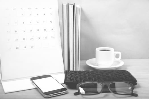 office desk : coffee with phone,stack of book,eyeglasses,wallet,calendar on wood background black and white color