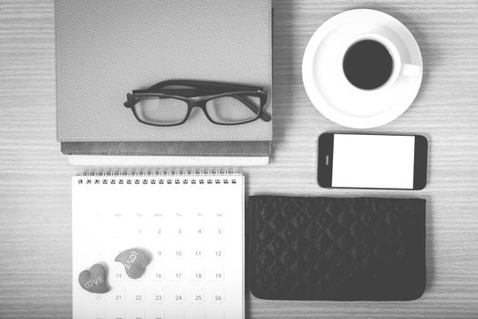 office desk : coffee with phone,stack of book,eyeglasses,wallet,calendar,heart on wood background black and white color