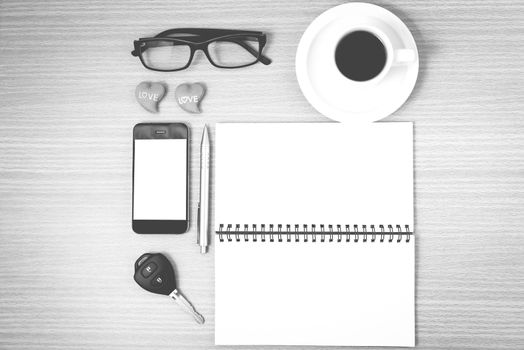 office desk : coffee and phone with car key,eyeglasses,notepad,heart on wood background black and white color