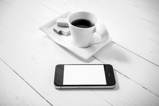 coffee cup with wafer and phone on white wood background black and white color