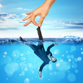 Businessman drowning in sea with big hand holding for leg