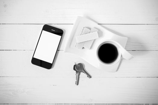 coffee cup with wafer,phone,key on white wood background black and white color