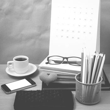 office desk : coffee with phone,wallet,calendar,color pencil box,stack of book,heart,eyeglasses on wood background black and white color