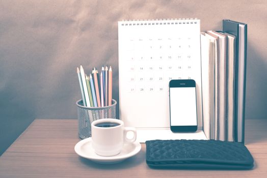 office desk : coffee with phone,wallet,calendar,color pencil box,stack of book on wood background vintage style