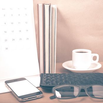 office desk : coffee with phone,stack of book,eyeglasses,wallet,calendar on wood background vintage style