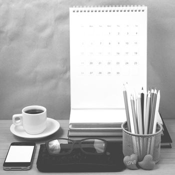 office desk : coffee with phone,wallet,calendar,color pencil box,stack of book,heart,eyeglasses on wood background black and white color