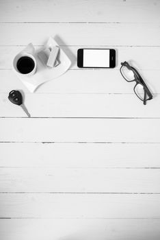 coffee cup with wafer,phone,car key,eyeglasses on white wood background black and white color