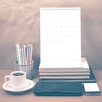 office desk : coffee with phone,wallet,calendar,color pencil box,stack of book on wood background vintage style