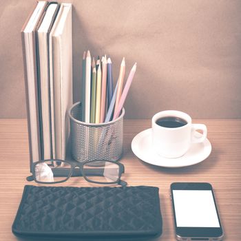 office desk : coffee with phone,stack of book,eyeglasses,wallet,color pencil box on wood background vintage style