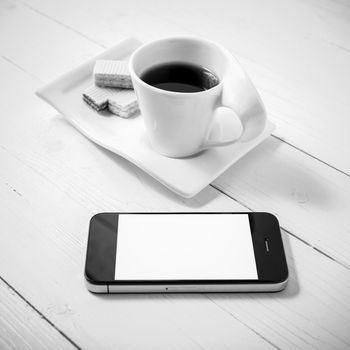 coffee cup with wafer and phone on white wood background black and white color