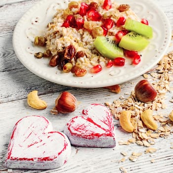 Cooked oat cereal with fruit and nuts on a background of two wooden hearts