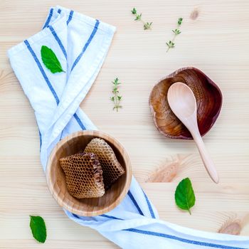 Honeycomb in wooden bowl with herbs mint ,thyme and sage set up on white wooden background.