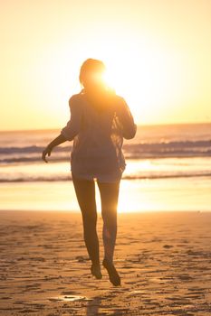 Happy woman enjoying isummer, running joyfully on beach in sunset.