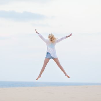 Relaxed woman enjoying freedom, feeling happy. Serene relaxing woman in pure happiness and elated enjoyment, jumping with arms outstretched up. Copy space for text.