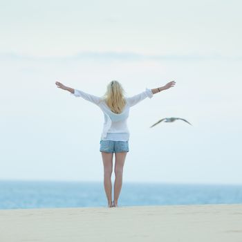 Woman enjoying freedom feeling as a bird at beach at dusk. Serene relaxing woman in pure happiness and elated enjoyment with arms raised outstretched up. 