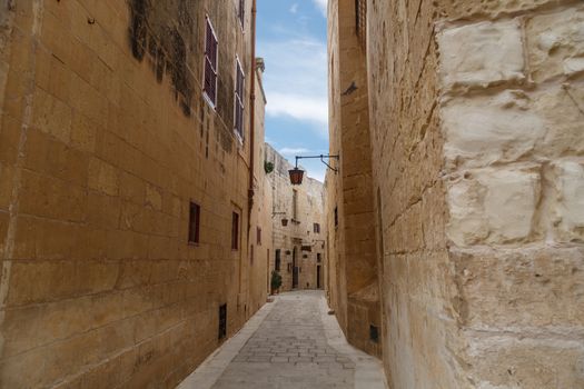 View of Mdina streets with limestone historical buildings around, on cloudy sky background.