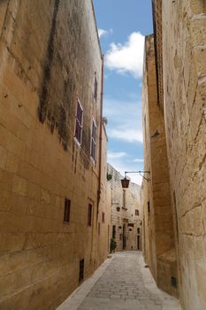 View of Mdina streets with limestone historical buildings around, on cloudy sky background.