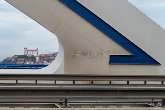 Shape of a modern bridge Apollo with a blue detail. In the background the downtown of Bratislava with the castle and cathedral. Intensively cloudy sky.