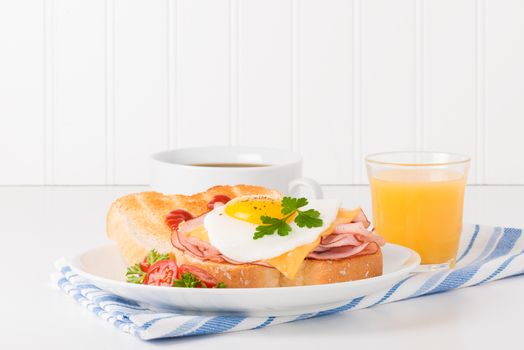 Delicious sandwich of fried egg, ham and cheese served with coffee and juice.
