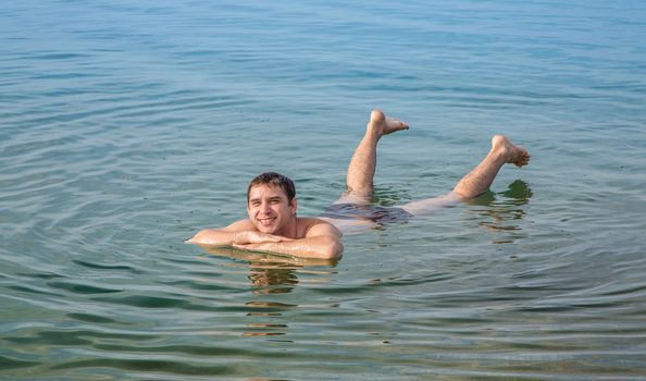 Man floating in the Dead Sea in Jordan. Dense salty water pushes the man out. Smiling man swims in the sea.