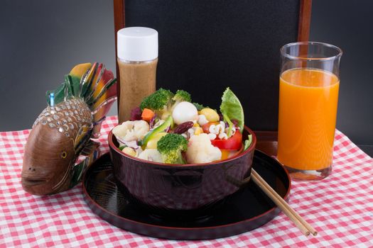 Vegetable salad with oriental sesame salad dressing with a glass of orange juice and a small black board background.