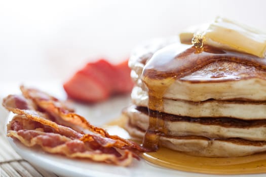 Pancakes with butter and honey served with bacon and strawberries