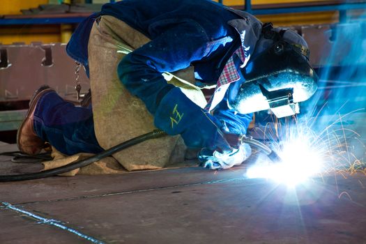 Man welding dressed in blue wearing protective clothes and equipment