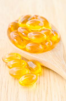 Fish oil capsules in wooden spoon on wooden background.