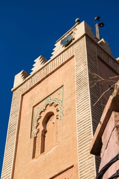 Minaret of one of many mosques in the medina of Marrakesh, enlightened by sun. Traditional architectural details. Bright blue sky.