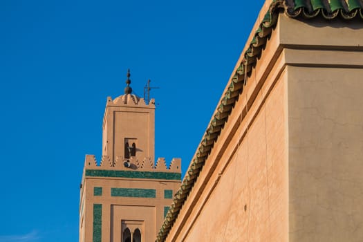 Minaret of one of many mosques in the medina of Marrakesh, enlightened by sun. Traditional architectural details. Bright blue sky.