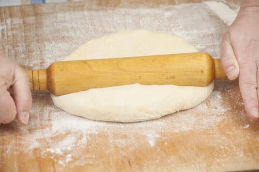 Hands baking dough with rolling pin on wooden table, depth of field